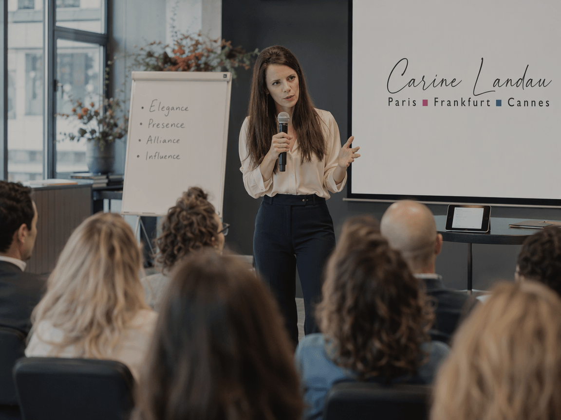 Carine Landau speaking with a handheld microphone to a seated audience at a corporate keynote